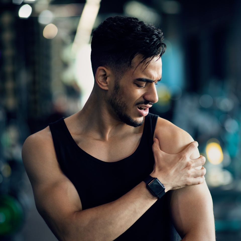 Sports Injury. Young Middle Eastern Man Suffering Shoulder Pain During Training At Gym, Arab Male Athlete Having Acute Muscle Ache, Touching Painful Area And Frowning, Closeup Shot With Copy Space
