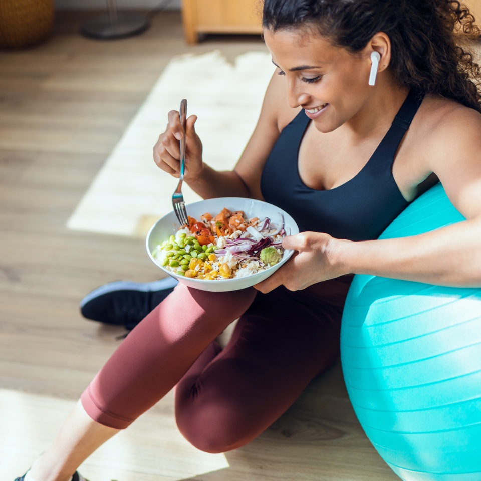 Shot of sporty young woman eating healthy while listening to music sitting on the floor at home.