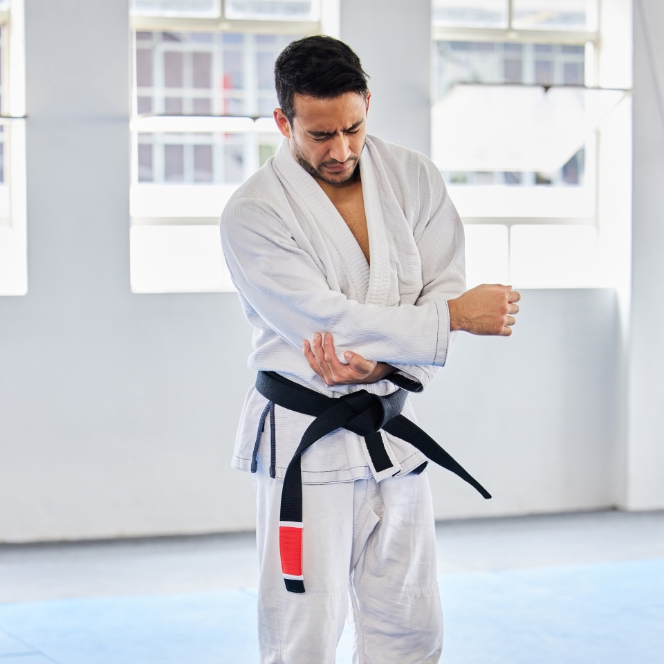 Karate injury, hurt and elbow pain for a man athlete holding painful arm at the gym. Active, Sport and athletic male suffering from muscle inflammation due to an exercise, fight training or workout.