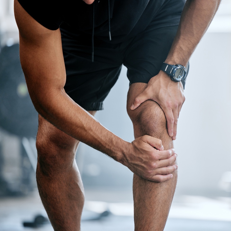 Fitness, gym and mockup, man with knee pain and medical emergency from workout injury at sports studio. Exercise, health and wellness, bodybuilder with hand on leg muscle ache for relief at training