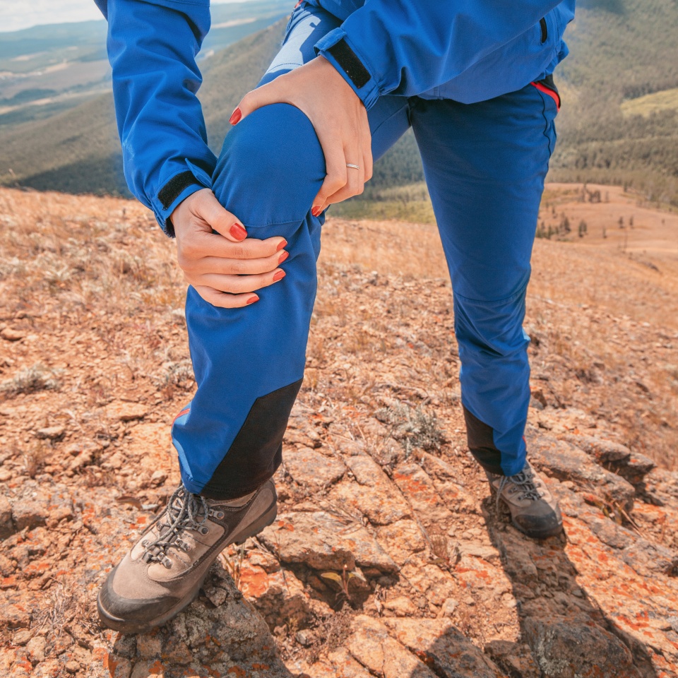 Woman is holding on to the knee joint, suffering from acute pain. Concept of injury of meniscus during a hike in the highlands