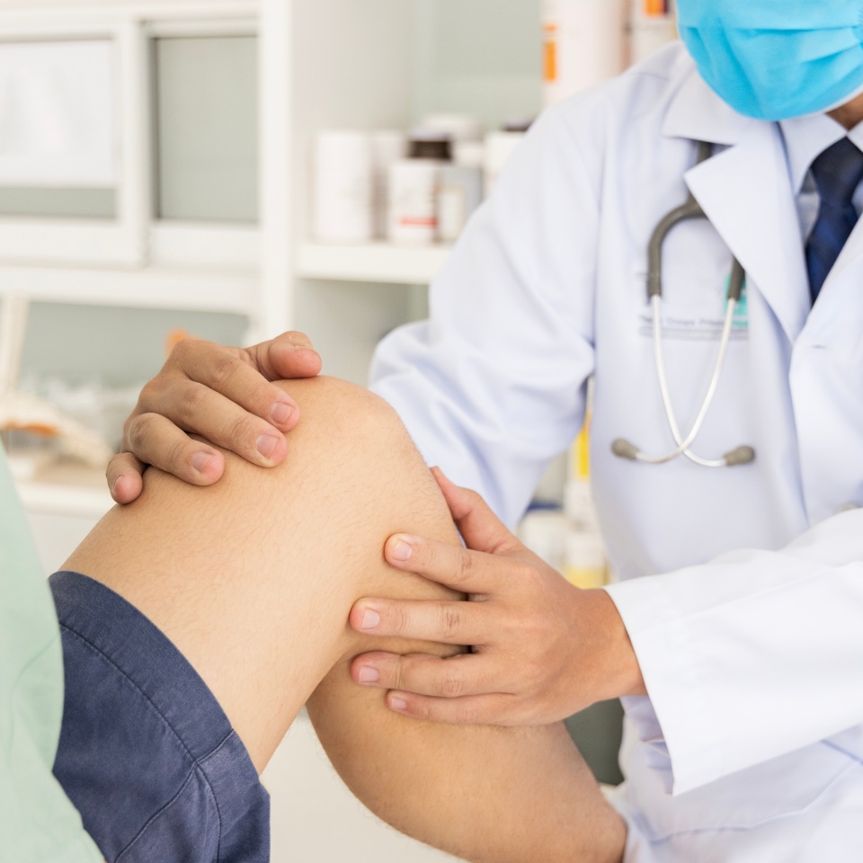 The orthopedic doctor or surgeon in white gown examined the patient with knee pain problem.White clean table or bed with blur background.Knee ligament or meniscus sport injury.Orthopaedic unit.