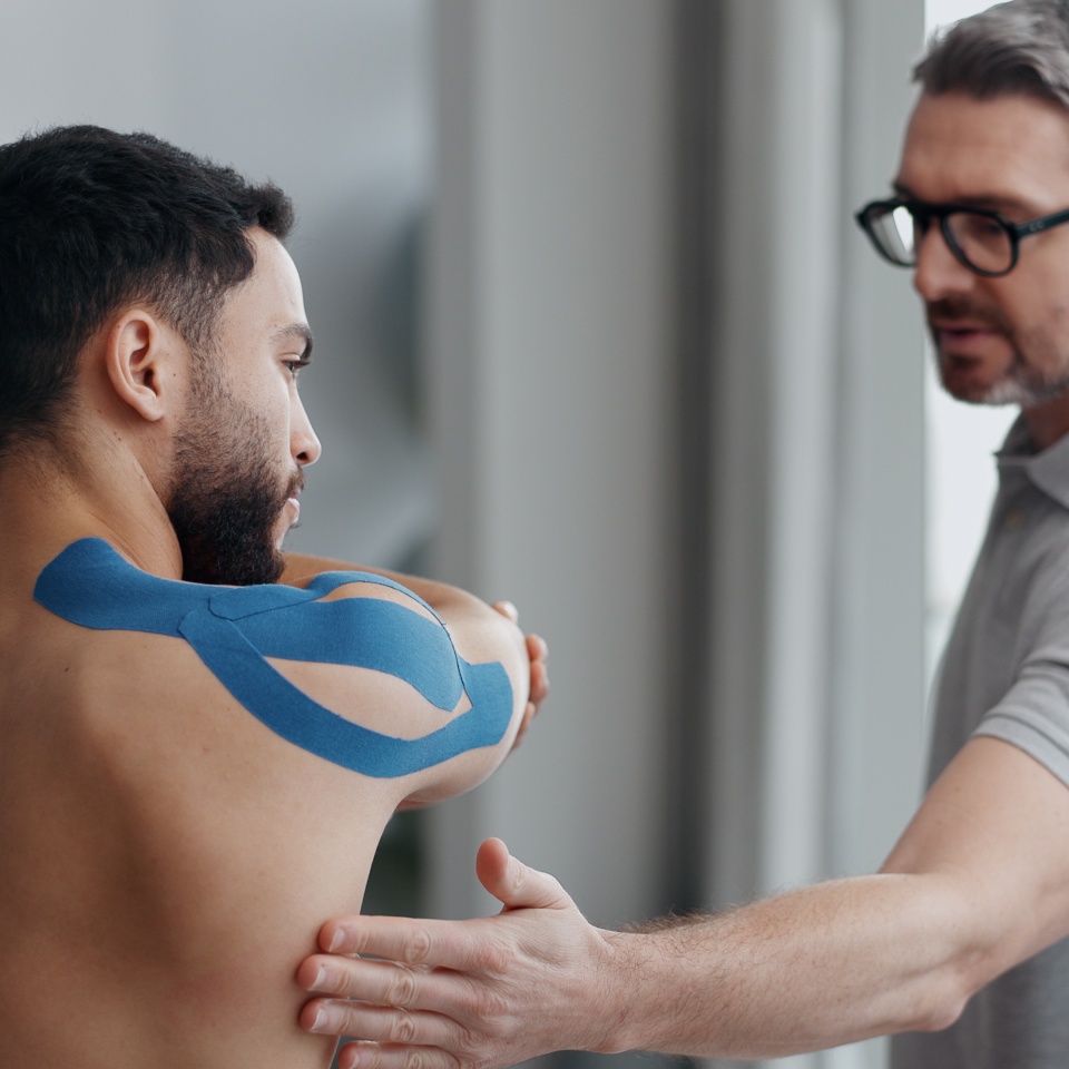Physiotherapist, man and stretching with tape for recovery, injury and guide for health at clinic. People, help and support with exercise for shoulder pain with muscle in rehabilitation at hospital.