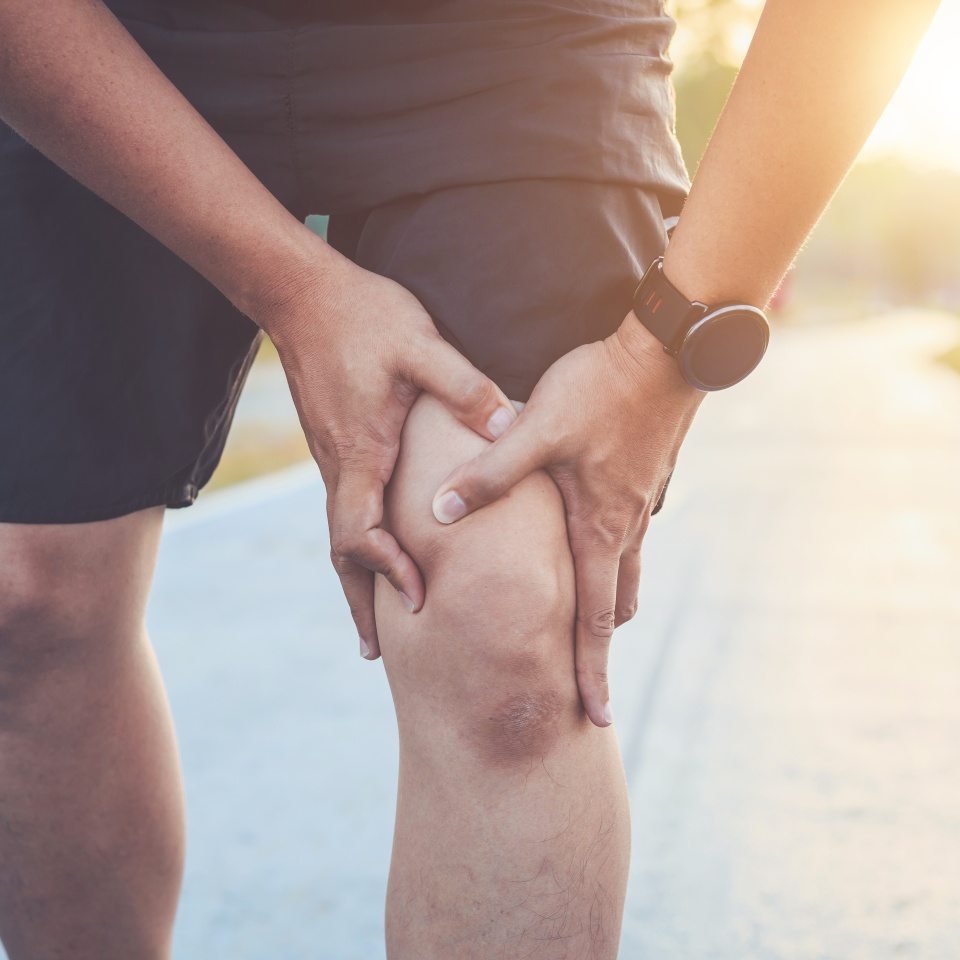 Injury from workout concept : The asian man use hands hold on his knee while running on road in the park. Shot in morning time, sunlight and warm effect with copy space for text or design