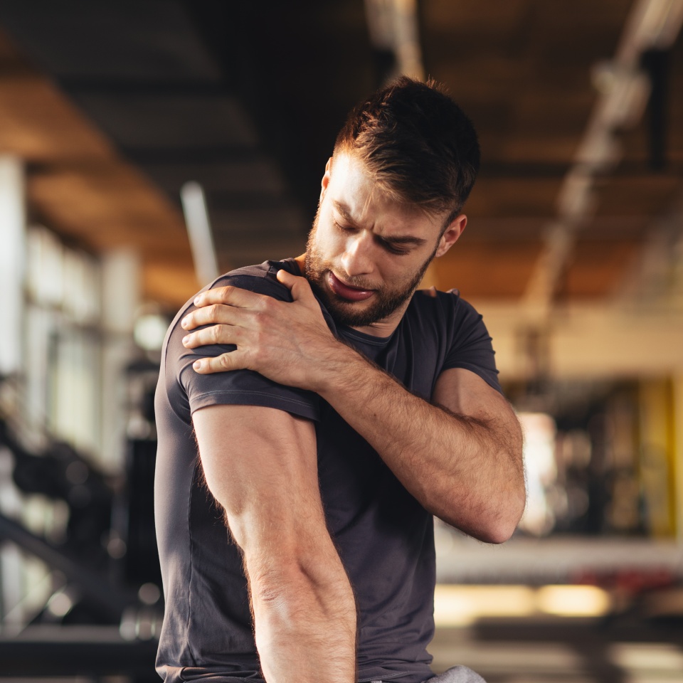 Handsome young man feeling the pain in shoulder at the gym