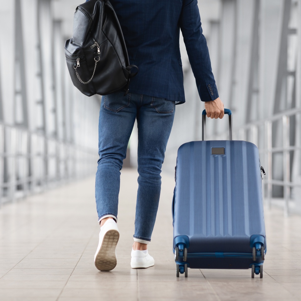 Unrecognizable Man With Bag And Suitcase Walking In Airport Terminal, Rear View Of Young Male On His Way To Flight Boarding Gate, Ready For Business Travel Or Vacation Journey, Cropped, Copy Space