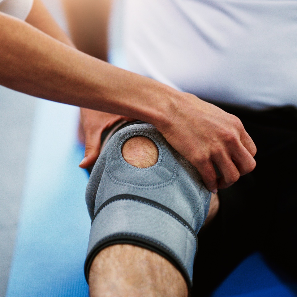 Physiotherapist hands, knee brace and man with injury, pain and torn muscle. Physiotherapy, male patient and female medical professional help, consulting and rehabilitation for leg and healthcare