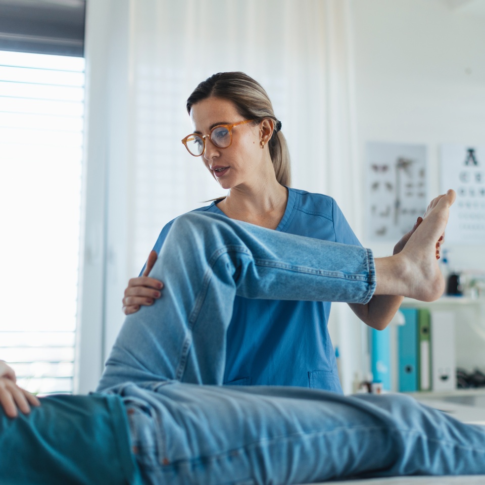 Physiotherapist doing manual therapy, exercise with teenage boy's knee, rehabilitation. Orthopedist examining and treating painful injured knee of young athlete. Concept of teen preventive health care.