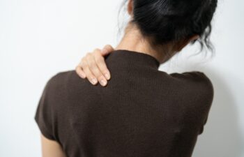 office syndrome in office worker concept. A person with dark hair reaches back to touch their shoulder, expressing discomfort or tension.