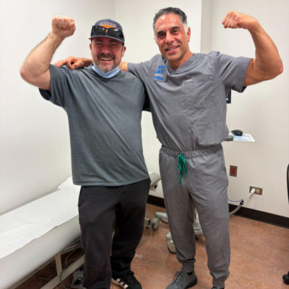A smiling man in a baseball cap and a man in medical scrubs pose side-by-side with their arms flexed.