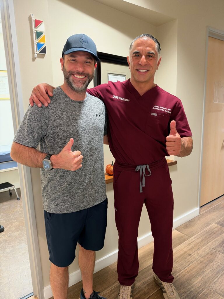 A patient and his surgeon in medical scrubs posing together and giving thumbs-up.