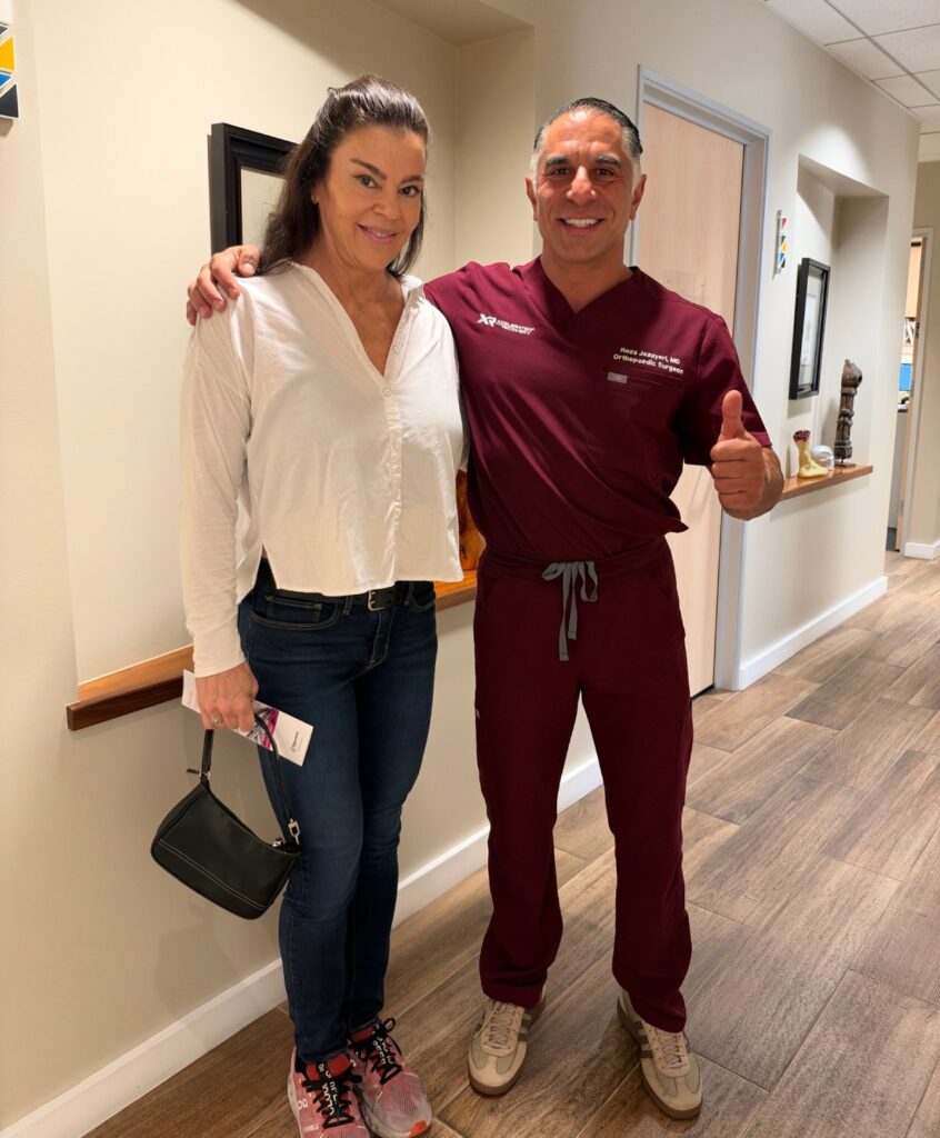 A woman standing next to an orthopaedic surgeon in maroon scrubs giving a thumbs up.